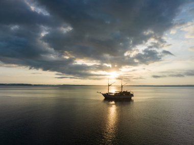 Endonezya 'nın batısındaki Fak Fak, Batı Papua yakınlarındaki Pasifik Okyanusu' nda bir Phinisi yelkenlisini aydınlatan sakin bir gün doğumu. Bu uzak tropikal alan olağanüstü deniz biyolojik çeşitliliğine ev sahipliği yapar..