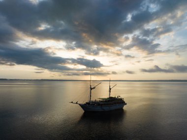 Endonezya 'nın batısındaki Fak Fak, Batı Papua yakınlarındaki Pasifik Okyanusu' nda bir Phinisi yelkenlisini aydınlatan sakin bir gün doğumu. Bu uzak tropikal alan olağanüstü deniz biyolojik çeşitliliğine ev sahipliği yapar..
