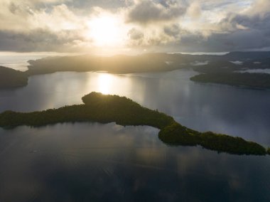 Gün ağarırken, Endonezya 'nın Raja Ampat kentindeki Batanta adasında alçak, güneşli bulutlar sürükleniyor. Bu bölge inanılmaz yüksek deniz biyolojik çeşitliliği nedeniyle Mercan Üçgeni 'nin kalbi olarak bilinir..