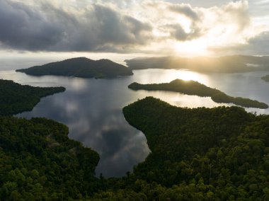 Gün ağarırken, Endonezya 'nın Raja Ampat kentindeki Batanta adasında alçak, güneşli bulutlar sürükleniyor. Bu bölge inanılmaz yüksek deniz biyolojik çeşitliliği nedeniyle Mercan Üçgeni 'nin kalbi olarak bilinir..