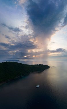 Gün doğarken yağmur bulutları Endonezya 'daki Ambon yakınlarında tropikal deniz manzarası boyunca sürükleniyor. Bu tropikal bölge sıradışı deniz biyolojik çeşitliliğine ev sahipliği yapar ve dalgıçlar ve şnorkelciler arasında popülerdir..