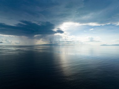 Yağmur bulutları, Endonezya 'da uzak bir adanın yakınlarında gün doğumunda sakin denizleri aşar. Bu güzel bölge, dalış ve şnorkelle dalış için popüler, olağanüstü deniz biyolojik çeşitliliği barındırıyor..