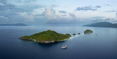 Dalış yapan bir yelkenli, Endonezya 'nın Raja Ampat kentindeki manzaralı kireçtaşı adalarının yakınında demirliyor. Bu uzak bölge zarif mercan resifleri ve genel deniz biyolojik çeşitliliği ile bilinir..