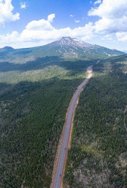 Clouds drift above Mt. Bachelor, Oregon, on a blue sky day during summer. This scenic mountain and its surrounding forests, near Bend, provide exceptional hiking, biking, climbing, and camping. clipart