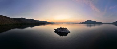 A colorful sunrise illuminates a ship near the beautiful island of Adoenara in the Lesser Sunda Islands of Indonesia. This area harbors high marine biodiversity and is part of the coral triangle.  clipart