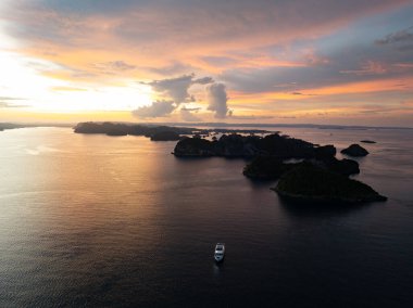 Misool, Raja Ampat 'ta kireçtaşı adaları alacakaranlıkta siluetlenir. Bu tropikal bölge, olağanüstü deniz biyolojik çeşitliliği nedeniyle dalgıçlar ve şnorkelliler için popüler bir yerdir..