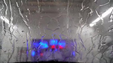 You look through the windshield of a car as the car is rinsed in a car wash and driven into the dry area. Drops move on the windshield.