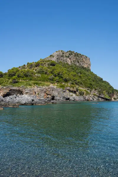 İtalya 'nın Calabria şehrinde Arco Magno yakınlarında yer alan Praia' daki Isola di Dino adası. Adada ağaçlar var. Ön planda su boyunca uzanan küçük taşlarla temiz mavi denizi ve güzel mavi gökyüzünü de görebilirsiniz. Metin için boşluk.