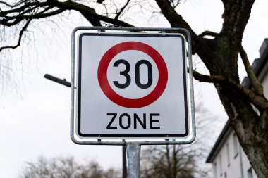30 km / s hız sınırı için sokak tabelası. Arka planda ağaçlar görülebilir. Trafik levhası bir direğe monte edilmiştir. Göstergede yansıtıcılar ve 30 sayısı var..