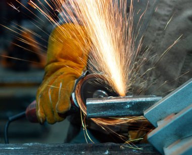 Koruyucu maskeli işçi atölyede metal öğütücü üzerinde çalışıyor..