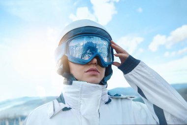 Dağların ve mavi gökyüzünün arkasındaki kayak merkezindeki kadın. Kayak maskesine yansıyan bir dağ sırası. Kış Sporları.