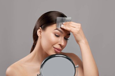 Beautiful woman using facial oil blotting paper.  Cosmetology, cosmetics. Facial treatment
