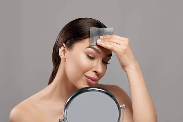 Beautiful woman using facial oil blotting paper.  Cosmetology, cosmetics. Facial treatment