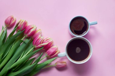 Bouquet of pink tulips on pink background. Two cups of hot, morning coffee in the shape of the number 8. Copy space. Mothers day