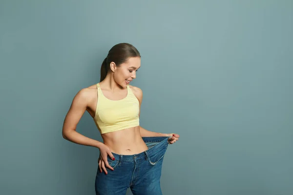 Woman showing result after weight loss wearing on old jeans on blue background. Dieting. Diet concept