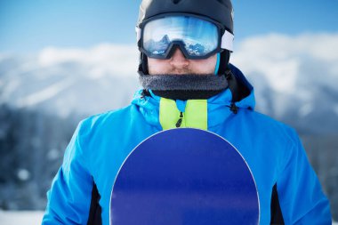 Kayak merkezindeki snowboardcu. Arka plandaki mavi gökyüzünde. Snowboard yapma. Kayak gözlüğü takıyor. Kar Dağlarının Yansımasıyla Kayak Gözlükleri