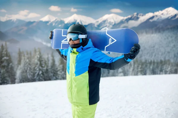 山と青い空の背景に男の肖像画 スノーボードを保持し スキーグラスを着用しています 雪山の反射でスノーボーダーのスキーゴーグル ウィンタースポーツ ストック画像