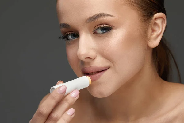 Beautiful Woman With Happy Face, Sexy Full Lips Applying Lip Balm from Stick. Portrait Of Female Model With Natural Makeup.