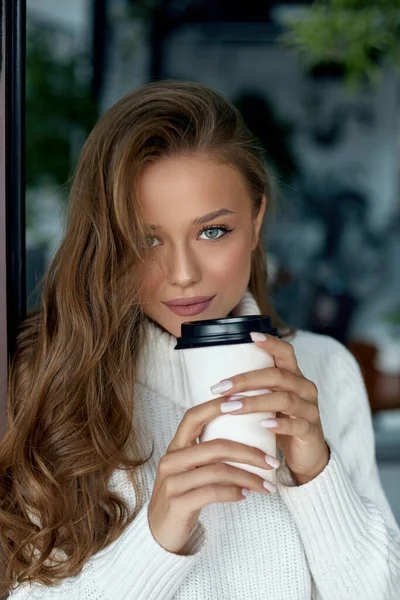 Beautiful woman drinking coffee. Girl holds paper cup of hot latte.