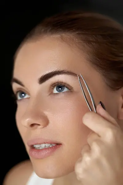 Eyebrow correction.  Plucking eyebrows. Beautiful young woman with tweezers. Model with beauty Face.  Natural Makeup