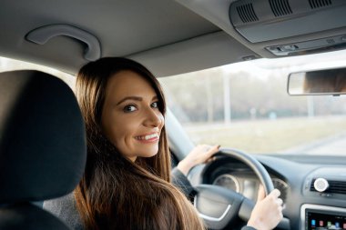 Kadın sürücüsü. Araba sürerken arkasını kollayan çekici genç bir kadın. Sürücü yolcu koltuğuna dönüyor.