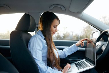 Arabada dizüstü bilgisayar ve telefon kullanarak güzel genç iş kadını