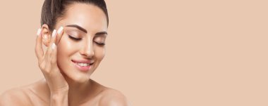 Beautiful smiling woman with healthy smooth facial clean skin applying cosmetic cream and touch own face. Model with  Beauty face. Skin care Moisturizer Facial treatment. Cosmetology. Spa.