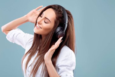 Stüdyoda kablosuz kulaklık kullanarak müzik dinleyen güzel bir kadın. Mavi arka planda izole edilmiş. Kablosuz kulaklıklardan ve danstan hoşlanan bir kız..
