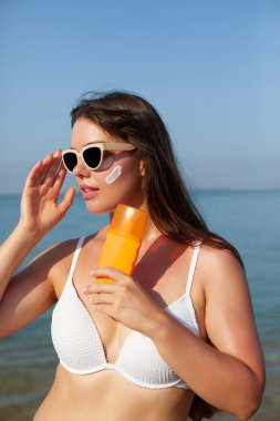 Güzel kadın tabaklanmış yüzüne krem güneş kremi uygulayarak. Güneş. Cilt ve vücut bakımı. Kız cildi için güneş kremi kullanıyor. Güneş losyonu tutan ve nemlendirici güneş kremi tutan bir kadın portresi.
