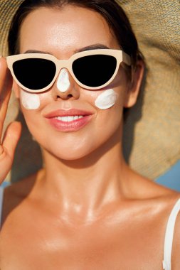 Kadın uygulanan güneş kremi yüzündeki gülümseme. Cilt Bakımı. Vücut güneş koruması. Güneş kremi. Kadın şapka smear losyon cildinize nemlendirici.