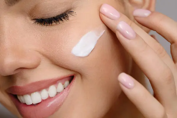 Güzel yüzlü bir kadın sağlıklı yüz portresine dokunuyor. Güzellik güzeli kız cilt bakımı ürünü uyguluyor. Sıvı kaybı. Krema lekesi. 