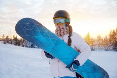 Dağların ve Günbatımının Arkasındaki Kadın Portresi. Snowboard tutuyor ve kayak gözlüğü takıyor. Kar Dağları 'nın yansıması olan kar kayakçısının kar maskeleri. Kış Sporları