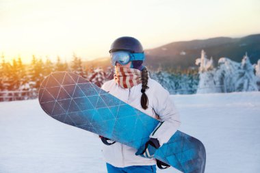Dağların ve Günbatımının Arkasındaki Kadın Portresi. Snowboard tutuyor ve kayak gözlüğü takıyor. Kar Dağları 'nın yansıması olan kar kayakçısının kar maskeleri. Kış Sporları