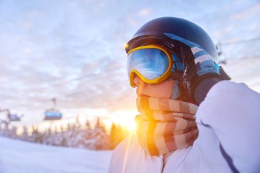 Günbatımı arka planında snowboardcu kadın. Kar maskesine yansıyan bir dağ sırası. Kış sporları. Kar gözlüklerini kapat, karlı dağların yansıması.