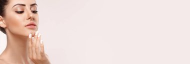 Yüzü temiz, güzel, gülümseyen bir kadın. Kozmetik krem sürüyor ve kendi yüzüne dokunuyor. Güzel yüzlü bir model. Cilt bakımı. Panorama