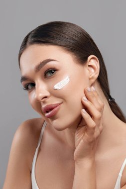 Güzel genç bir kadın yüzüne nemlendirici krem sürüyor. Temiz ciltli ve yüzüne dokunan bir güzellik modeli portresi. Spa, cilt bakımı ve sağlık. Yakın çekim, kopyalanma alanı.