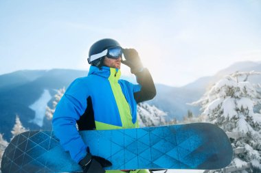 Arka plandaki kayak merkezinde kayak yapan adamın portresi snowboard yapıyor. Kayak gözlüğü takıyor.