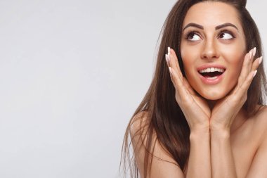 Şaşırmış ve şaşırmış bir kız ellerini kapatarak gülüyor. Doğal makyajlı güzel bir kadın. Ürünlerinizi sunuyor.