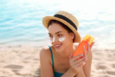 Güzel bir kadın bronzlaşmış yüzüne krem sürüyor. Güneş kremi. Deri ve vücut bakımı. 