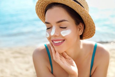 Güzel bir kadın bronzlaşmış yüzüne krem sürüyor. Güneş kremi. Deri ve vücut bakımı. Kız teni için güneş kremi kullanıyor.. 