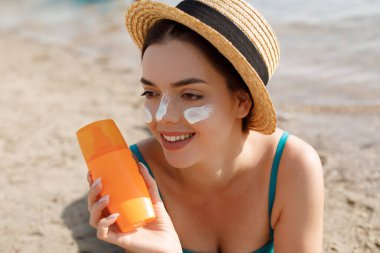 Güzel kadın tabaklanmış yüzüne krem güneş kremi uygulayarak. Güneş. Cilt ve vücut bakımı. Kız cildi için güneş kremi kullanıyor. Güneş losyonu tutan ve nemlendirici güneş kremi tutan bir kadın portresi.