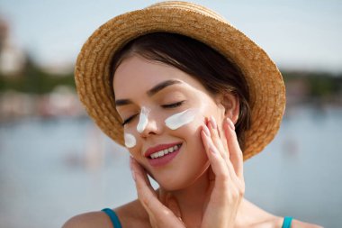 Kadın uygulanan güneş kremi yüzündeki gülümseme. Cilt Bakımı. Vücut güneş koruması. Güneş kremi. Kadın şapka smear losyon cildinize nemlendirici.