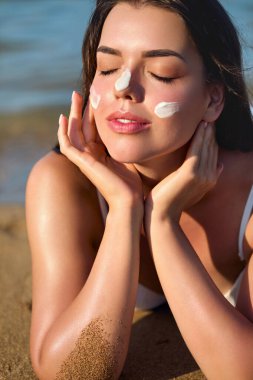 Cilt bakım konsepti. Vücut Güneşi koruması. Güneş kremi. Cilt üzerindeki kadın nemlendirici losyon. Yüzüne güneş kremi süren kadın gülüşü.