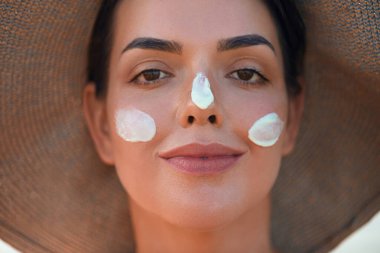 Yüzüne güneş kremi süren bir kadın gülümsemesi. Cilt bakımı. Vücut Güneşi koruması. Kadın kremi cilde nemlendirici losyon sürmüş. Güzel cilt bakımı konsepti.