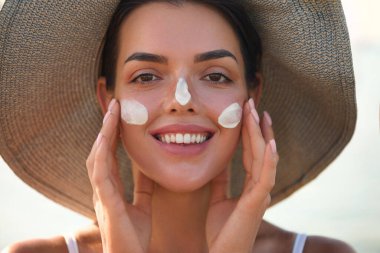 Güzel bir kadın bronzlaşmış bir yüze krem sürüyor. Güneş kremi. Deri ve vücut bakımı. Kız teni için güneş kremi kullanıyor.. 