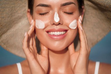 Güzel bir kadın bronzlaşmış yüzüne krem sürüyor. Güneş kremi kavramı... Deri ve vücut bakımı. Kız teni için güneş kremi kullanıyor. Cilt bakımı kavramı.