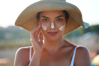 Yüzüne güneş kremi süren bir kadın gülümsemesi. Cilt bakımı. Vücut Güneşi koruması. Güneş kremi. Ciltte kadın yağı nemlendirici losyon..