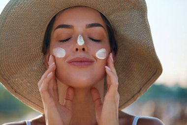 Yüzüne güneş kremi süren bir kadın gülümsemesi. Cilt bakımı. Vücut Güneşi koruması. Kadın kremi cilde nemlendirici losyon sürmüş. Güzel cilt bakımı konsepti.