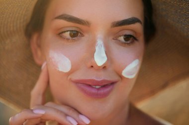 Yüzüne güneş kremi süren bir kadın gülümsemesi. Cilt bakımı. Vücut Güneşi koruması. Kadın kremi cilde nemlendirici losyon sürmüş. Güzel cilt bakımı konsepti.