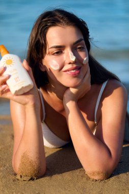 Yüzüne güneş kremi süren bir kadın gülümsemesi. Cilt bakım konsepti. Vücut Güneşi koruması. Güneş kremi. Ciltte kadın yağı nemlendirici losyon..